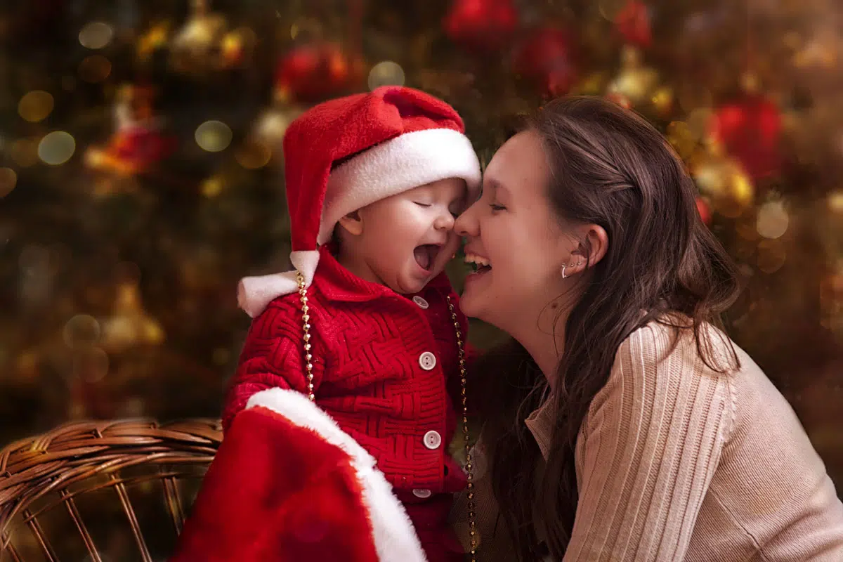 Femme avec un enfant portant des vêtements de Noël, avec un arrière-plan de décorations de Noël floues.