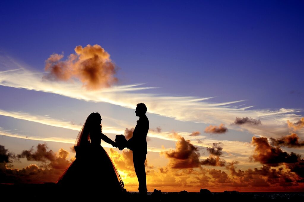 Un couple de mariés devant un ciel bleu avec des nuages.