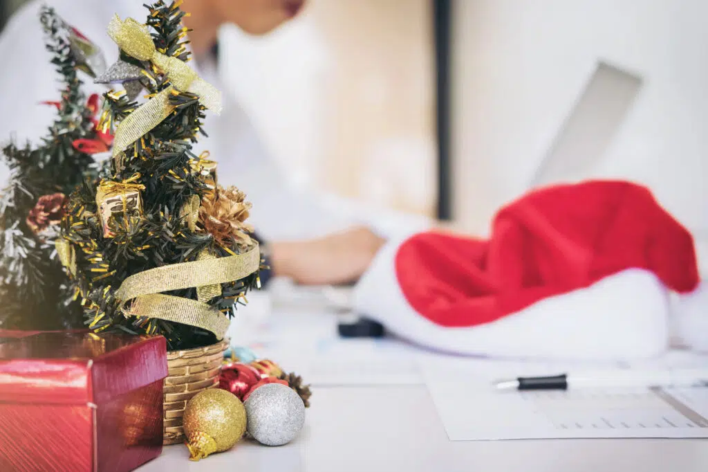 Sapin de Noël avec un chapeau de Noël sur un bureau d'entreprise. Une personne travaille sur un ordinateur au fond.